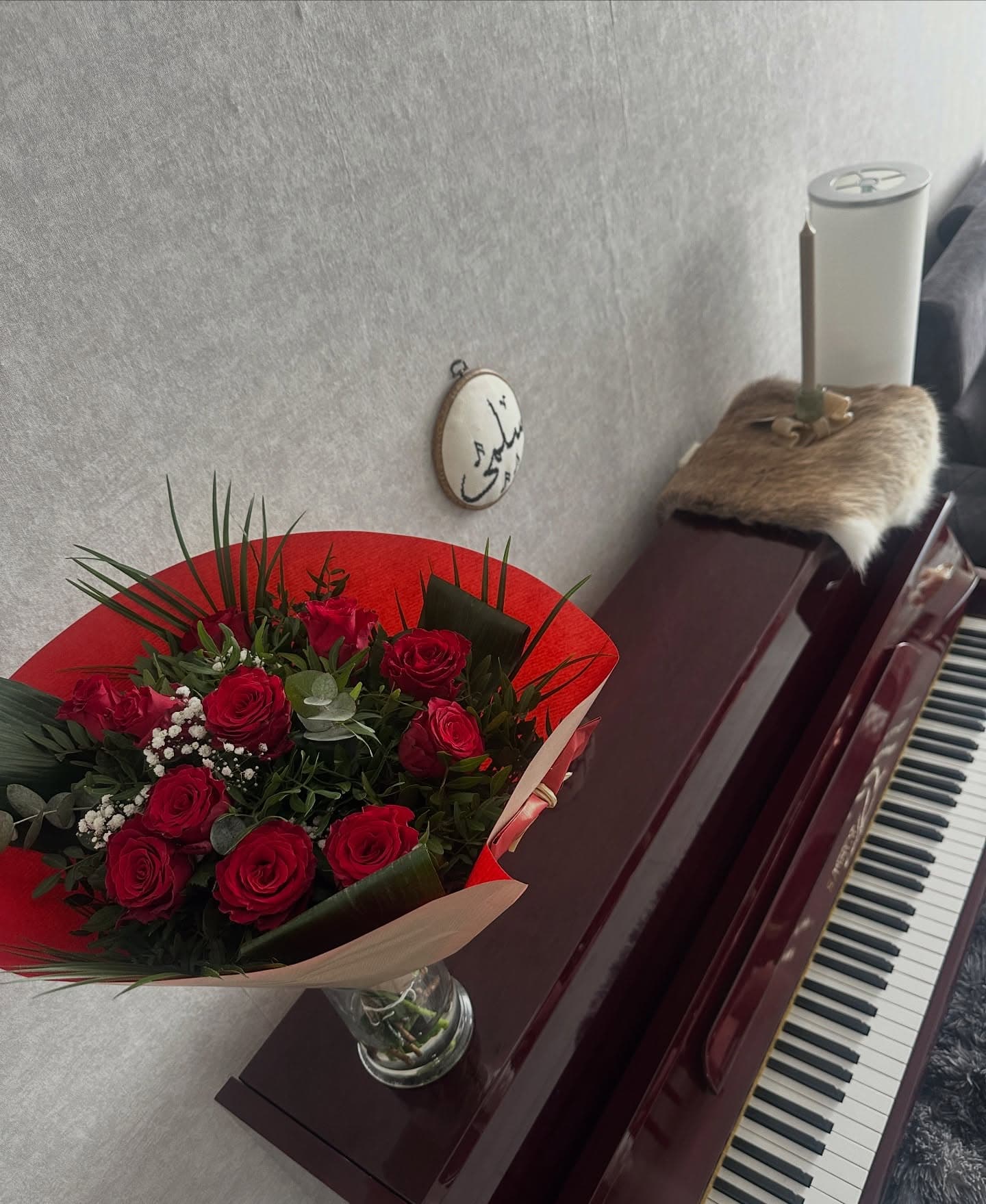 Boeket rode rozen naast de piano, met een borduurwerk van de naam Salma aan de muur